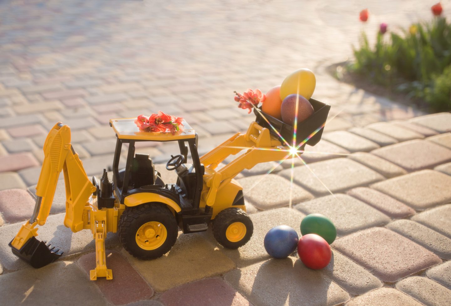toy excavator – a loader stands on the paving slabs, next to it – colorful Easter eggs